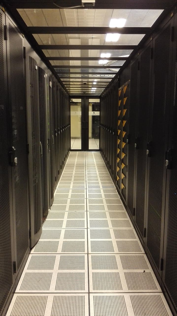 Corredor de data center com racks de servidores e piso elevado, luzes refletindo no teto