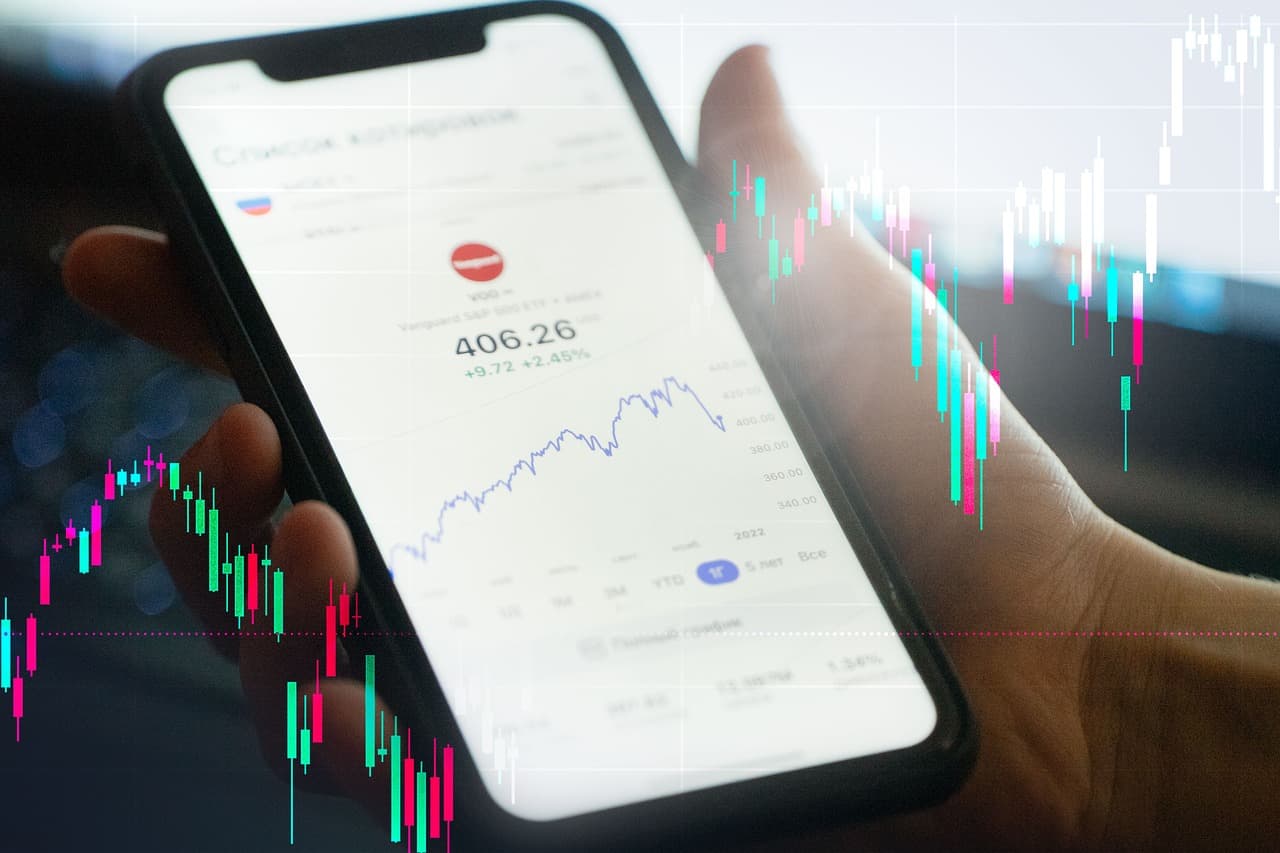 Mão segurando smartphone com gráfico financeiro e candles