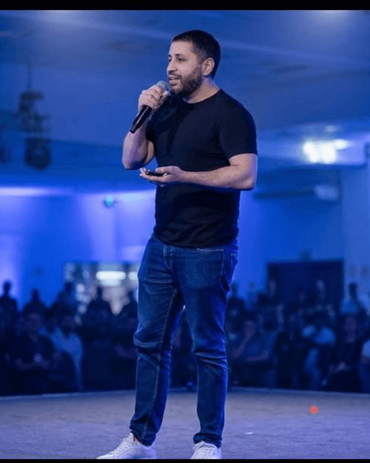 Danilo Gato palestrando em um auditório lotado, de microfone na mão