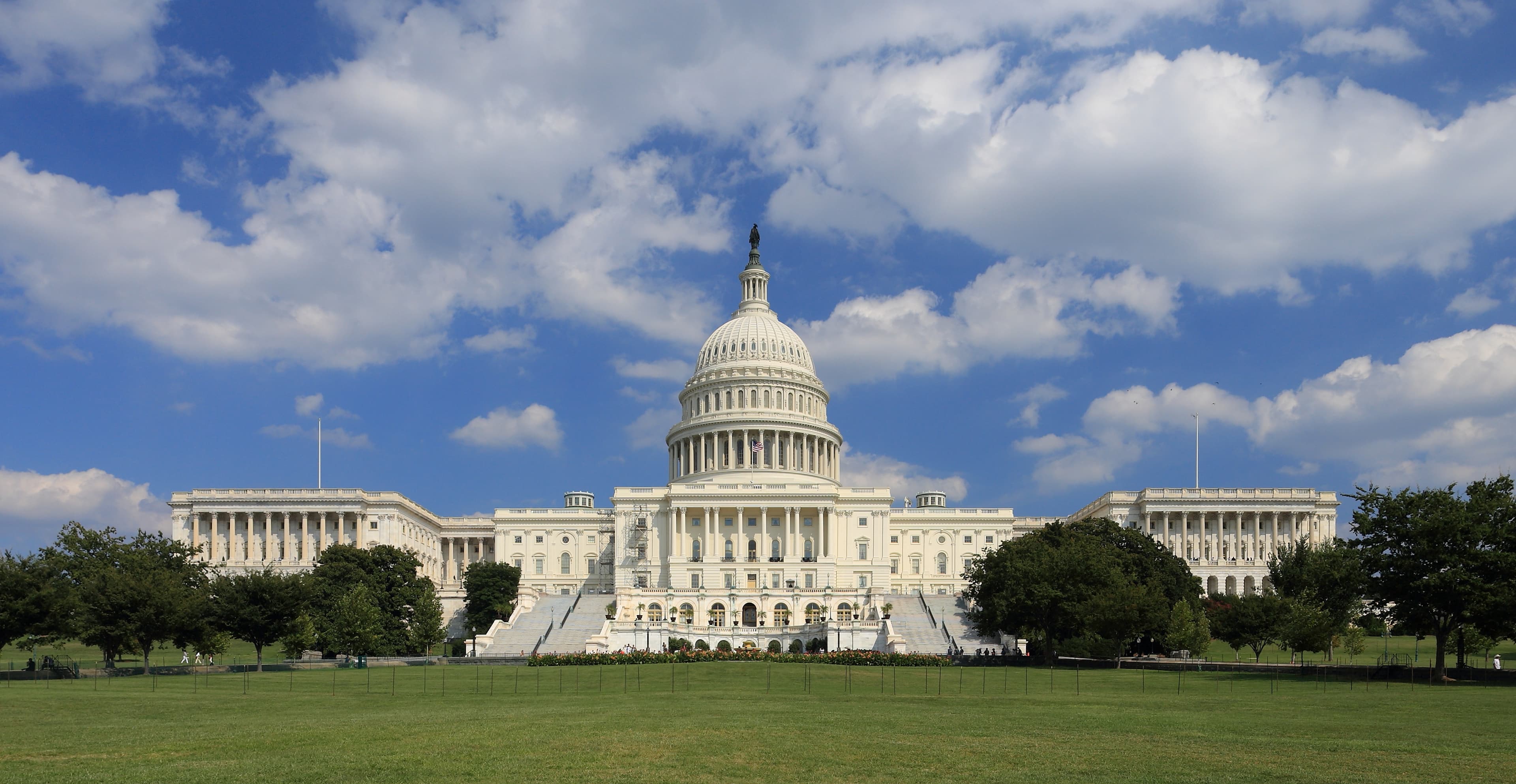 Fachada oeste do Capitólio dos EUA em Washington, céu azul e gramado em primeiro plano