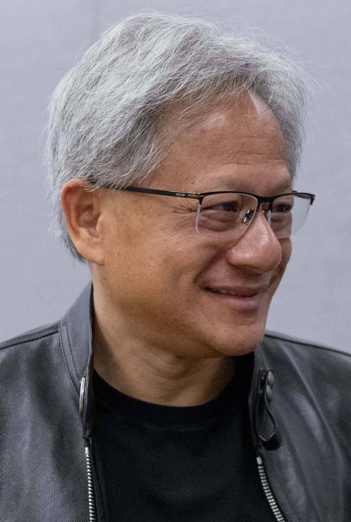 Jensen Huang em close, com jaqueta de couro preta, sorrindo