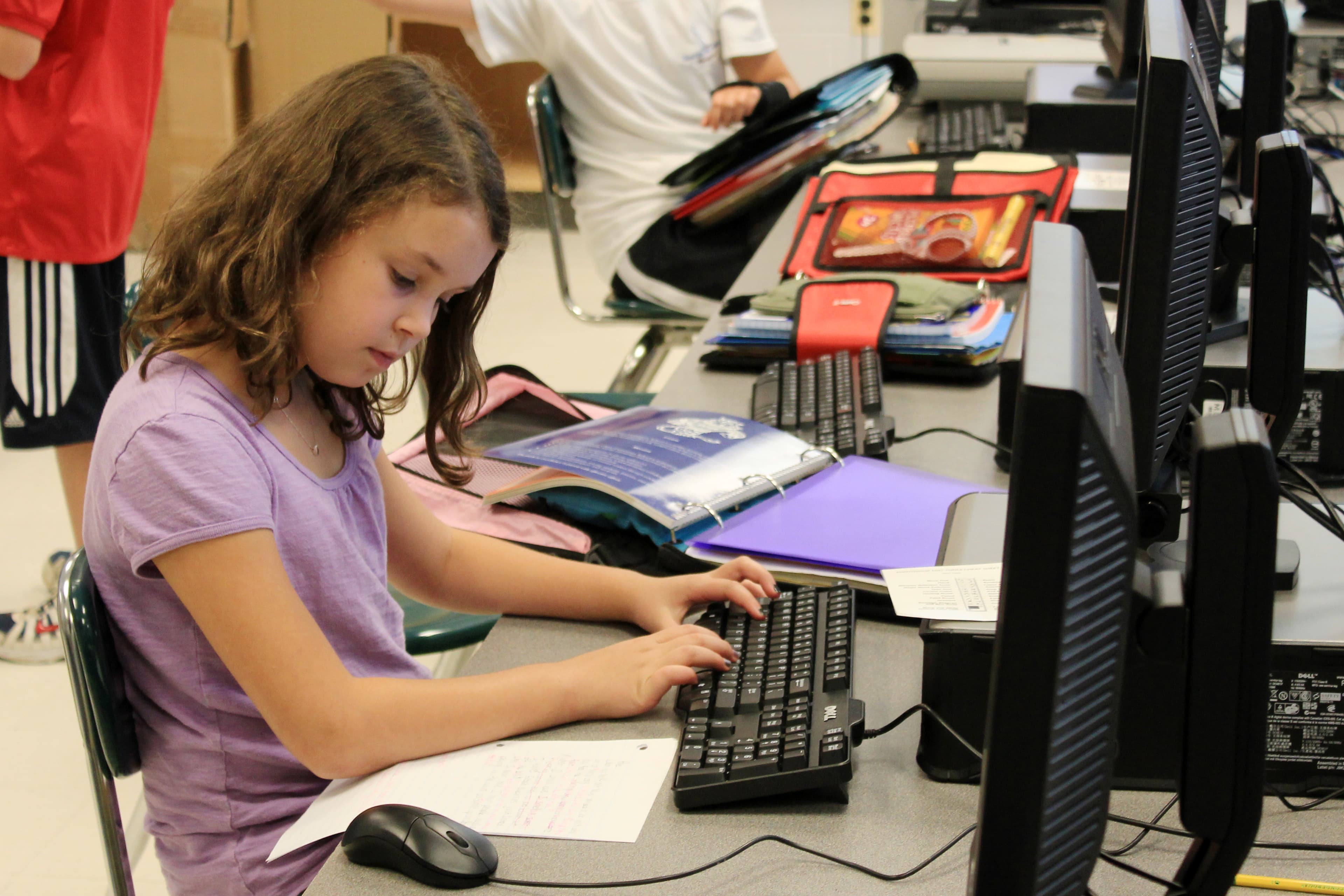 Aluna digitando em um computador em laboratório escolar