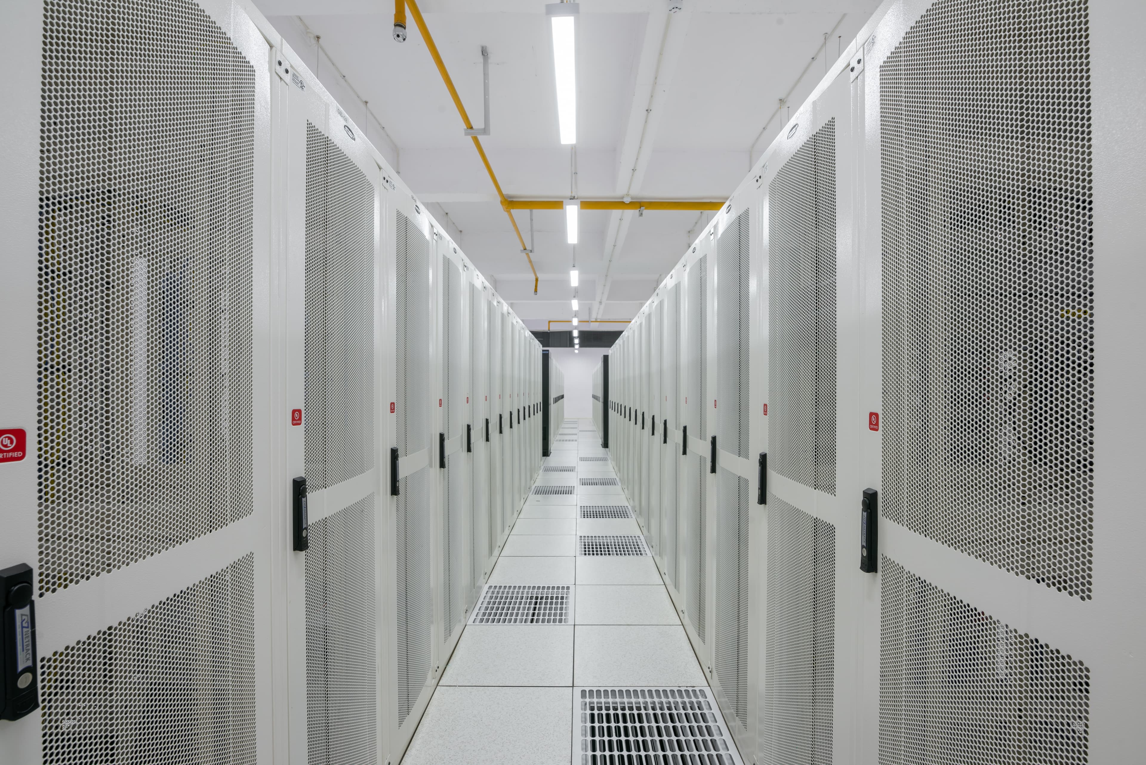 Corredor de racks de servidores em data center, iluminação fria e cabos organizados