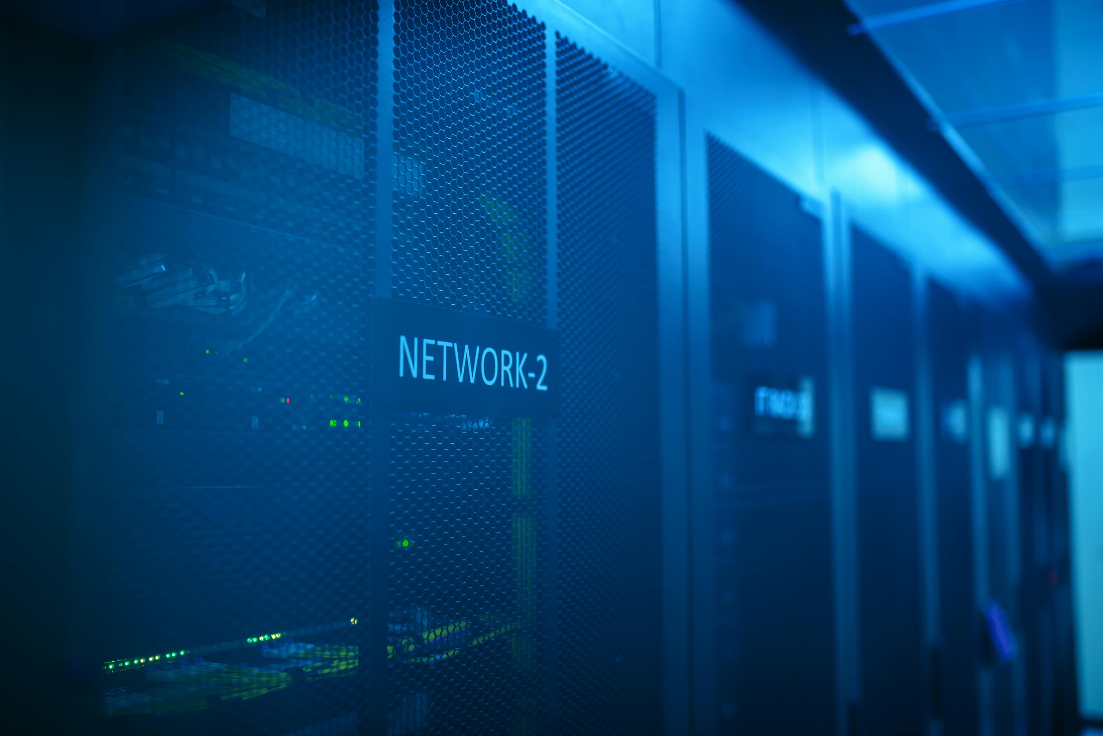 Corredor de data center com racks iluminados em azul, representando infraestrutura de nuvem