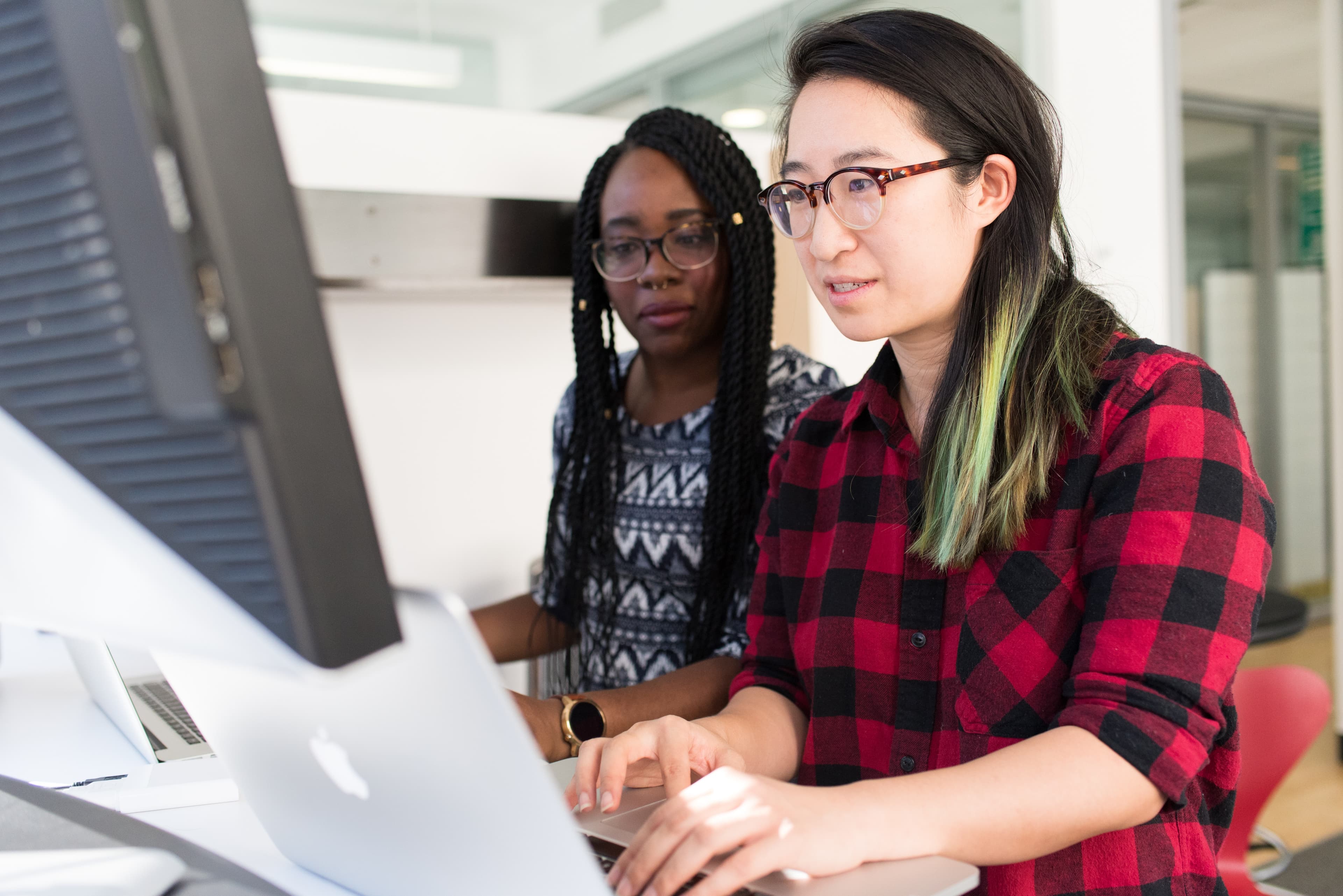 Duas engenheiras de software programando em um escritório, laptop e monitor visíveis