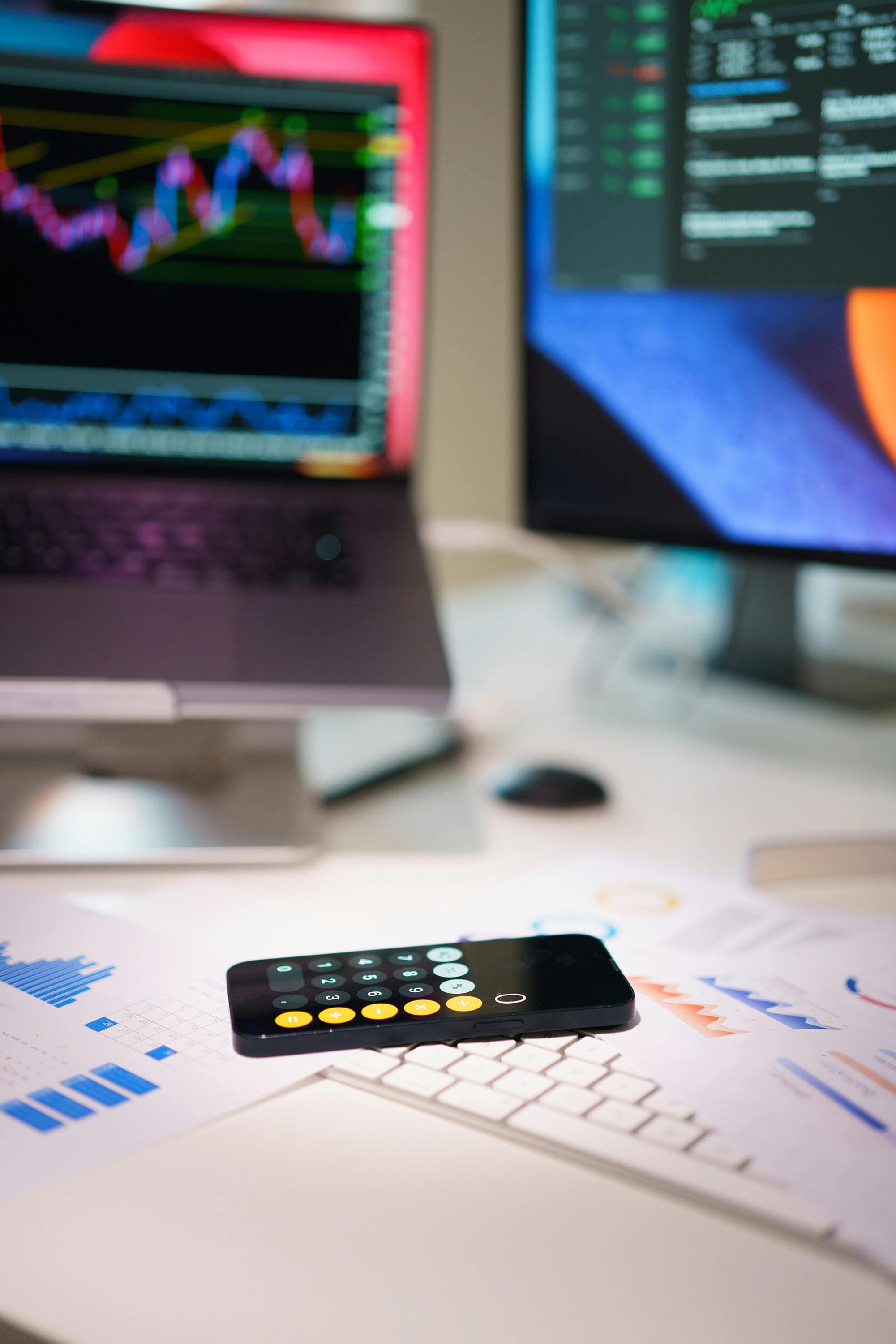 Mesa de trabalho com gráficos financeiros em telas e smartphone