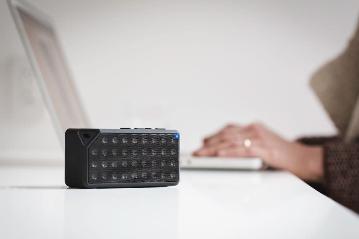 Alto-falante inteligente preto sobre mesa branca, em ambiente minimalista