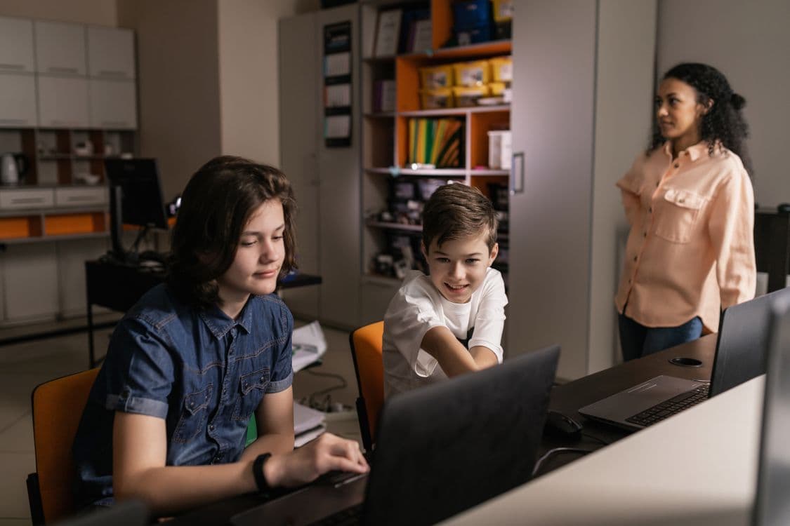 Alunos usando laptops em sala de aula com supervisão da professora