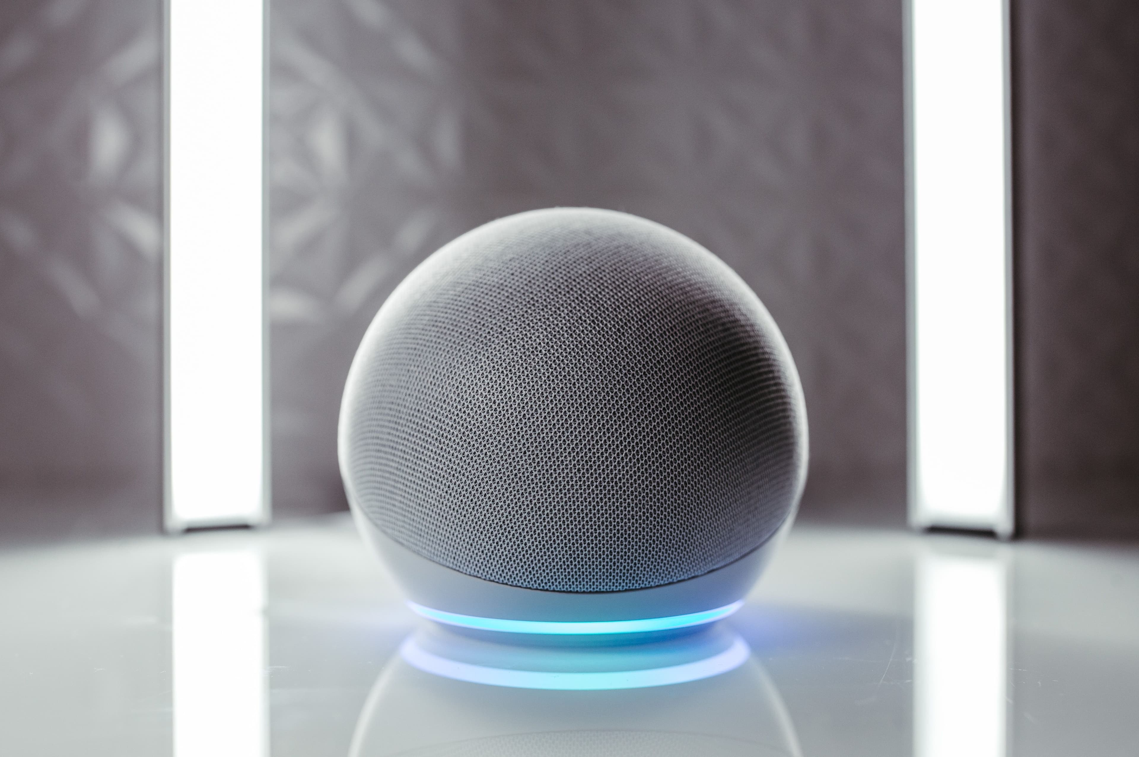 Smart speaker moderno com anel luminoso azul sobre superfície reflexiva