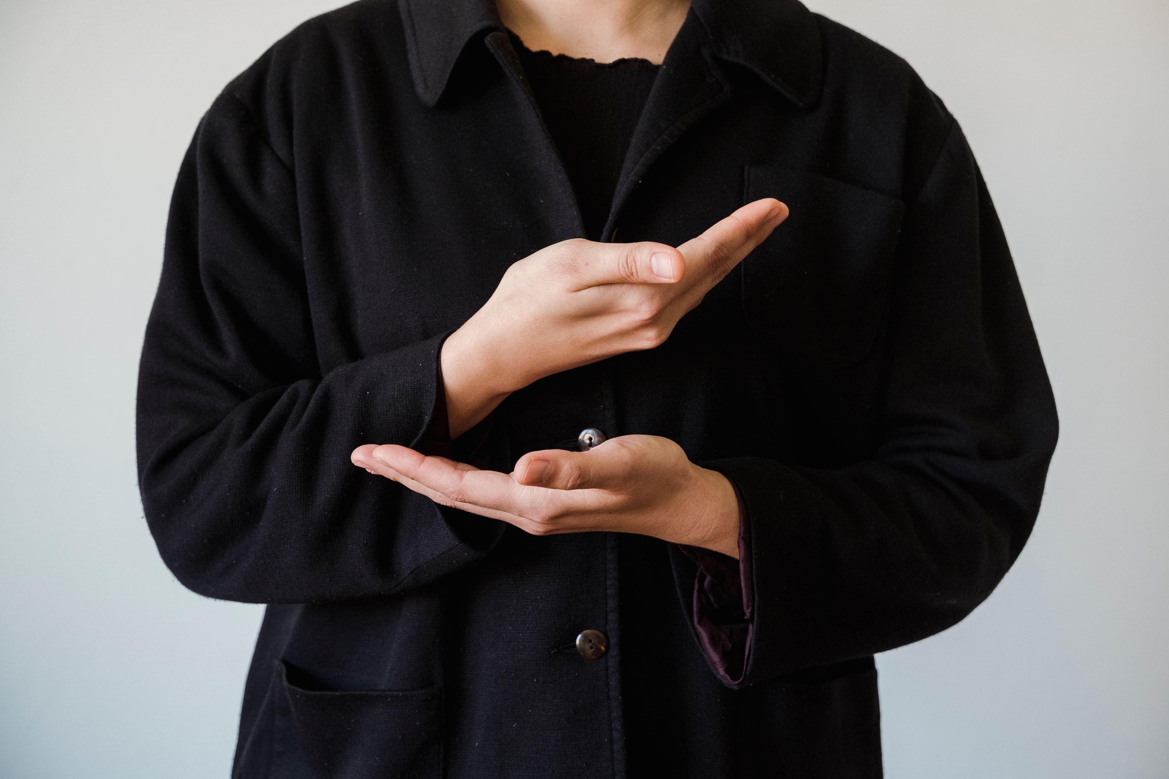 Pessoa sinalizando em ASL com as mãos em foco, fundo neutro