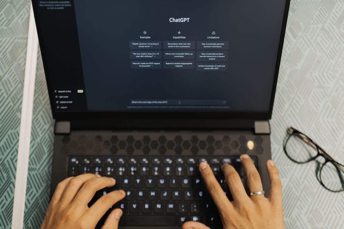 Mãos digitando em laptop exibindo a interface do ChatGPT