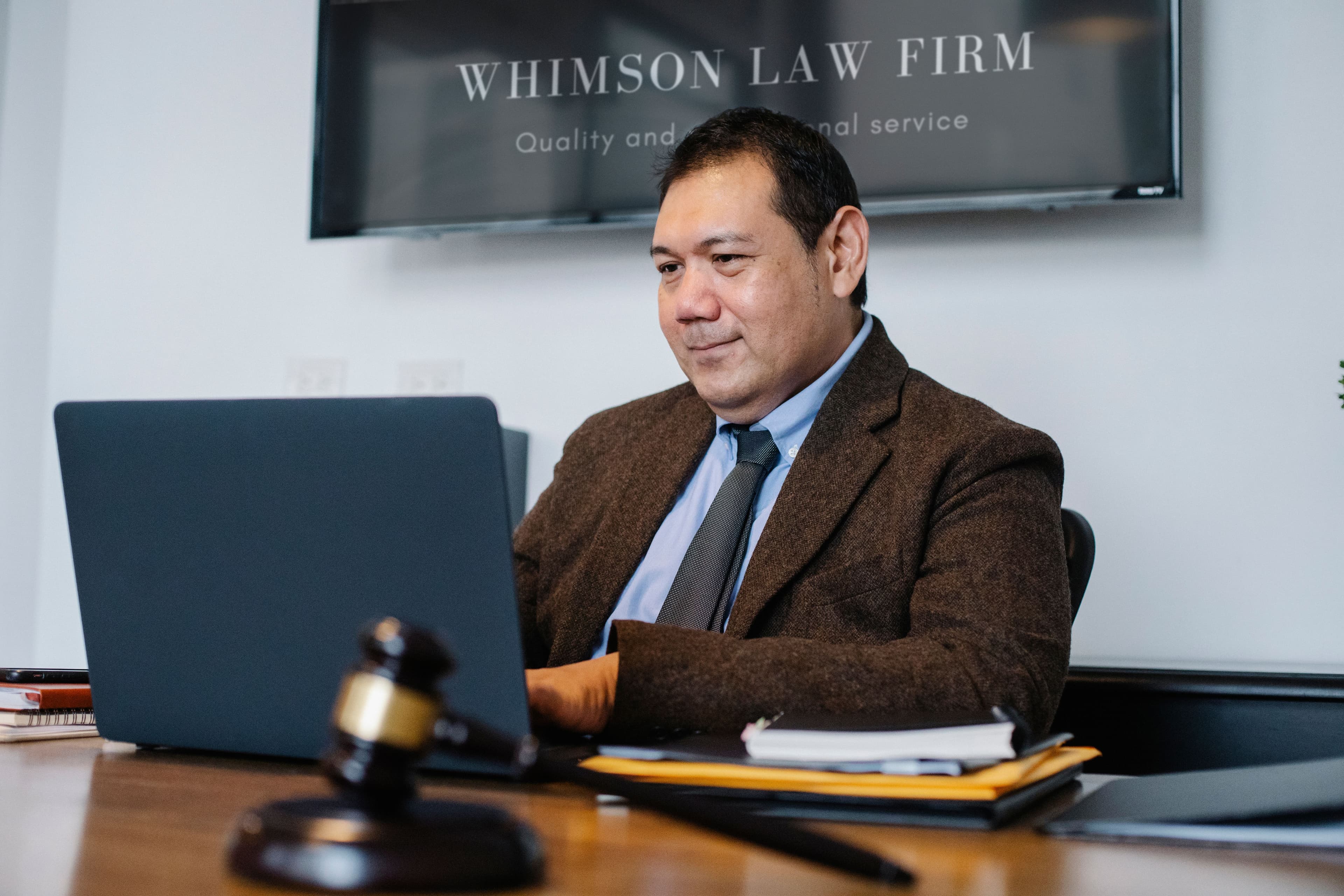 Gavel sobre mesa de madeira com advogado usando laptop ao fundo, simbolizando tecnologia jurídica