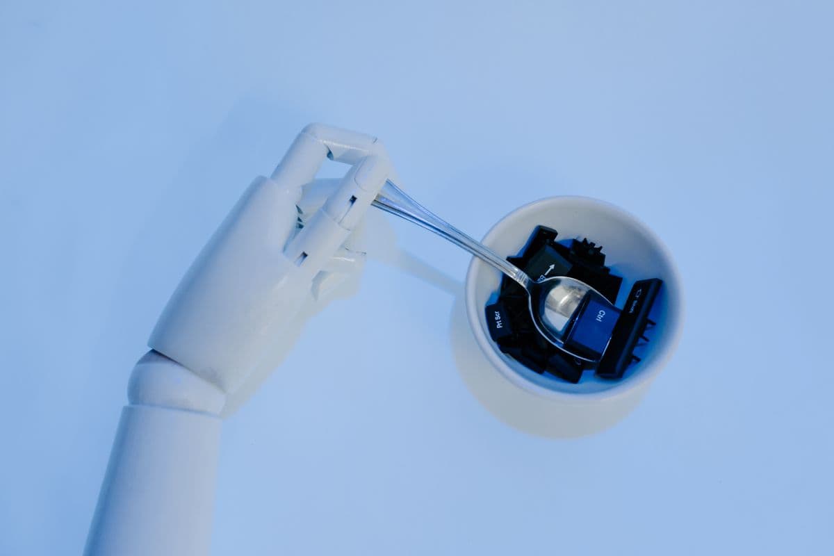 Mão robótica segurando colher com teclas de teclado, simbolizando IA e tecnologia