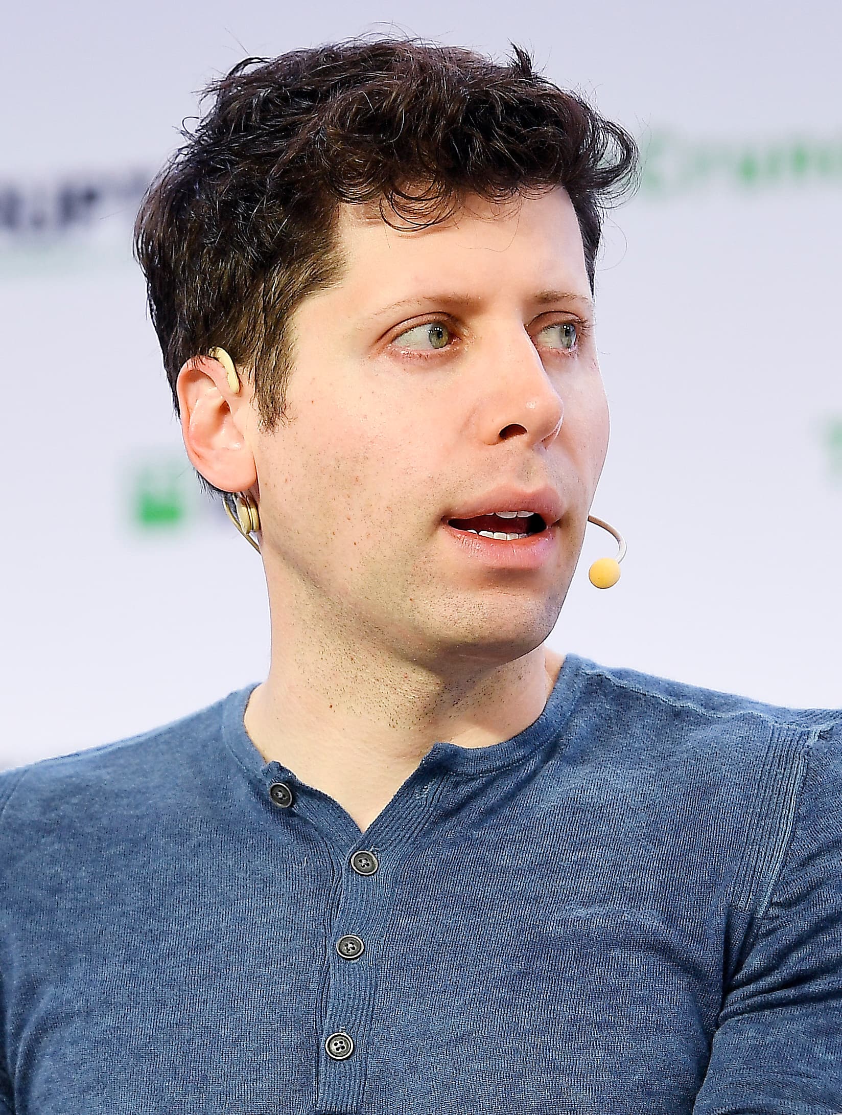 Sam Altman em evento de tecnologia, plano médio com microfone, fundo neutro